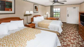 A hotel room with two beds, a desk, a television, and a ceiling fan.