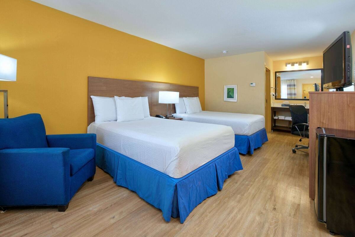 A hotel room with two beds, a desk, a chair, and a television.