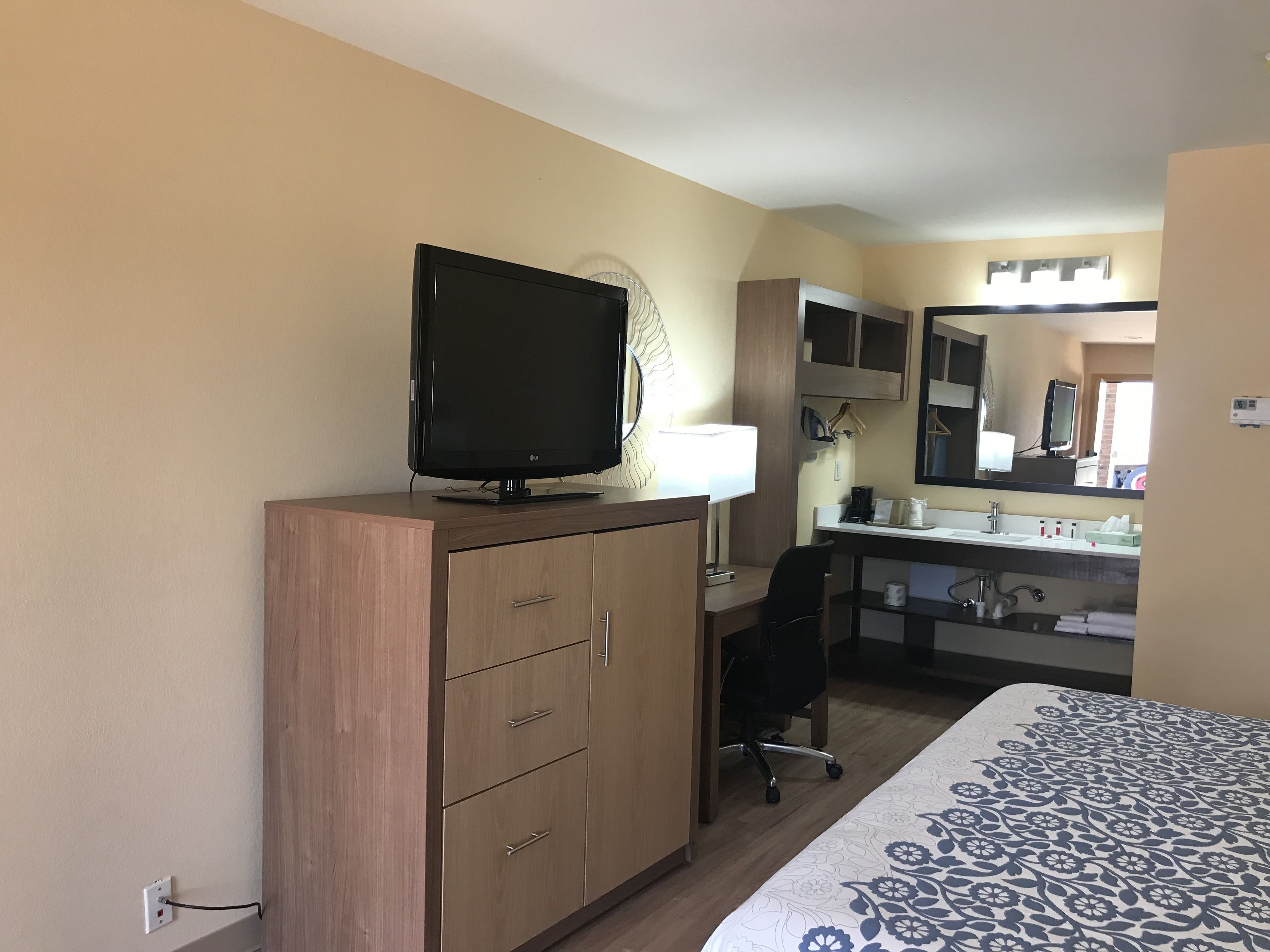 Une chambre d’hôtel comprenant un lit, un bureau avec un ordinateur, une télévision, un miroir et une armoire.