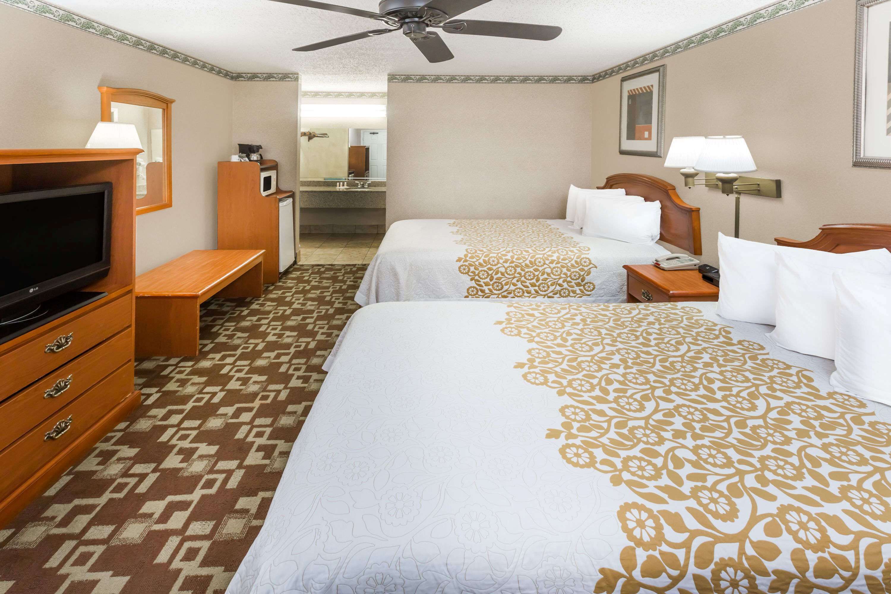 A hotel room with two beds, a TV, a desk, and a ceiling fan.