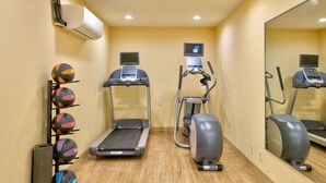 Ein Fitnessraum mit Laufbändern, Crosstrainern und einem Ballständer.