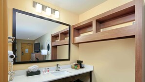 Ein Hotelbadezimmer mit großem Spiegel, Waschbecken, Fön, Handtuch und Ablagefläche für Pflegeprodukte.