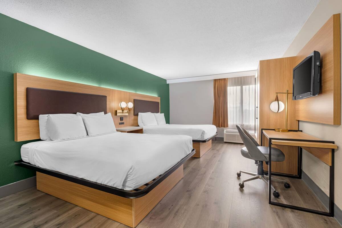 Une chambre d’hôtel avec deux lits, un bureau, une chaise, une télévision et une fenêtre avec des rideaux.