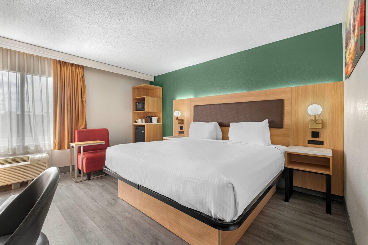 Une chambre d’hôtel avec un grand lit, un bureau, une chaise, un four à micro-ondes et un petit placard.