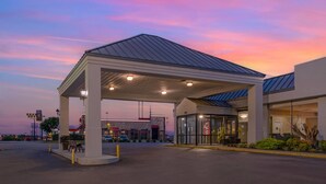 Una estación de servicio con marquesina cubierta, un edificio con acceso de vidrio y cielo despejado al atardecer.