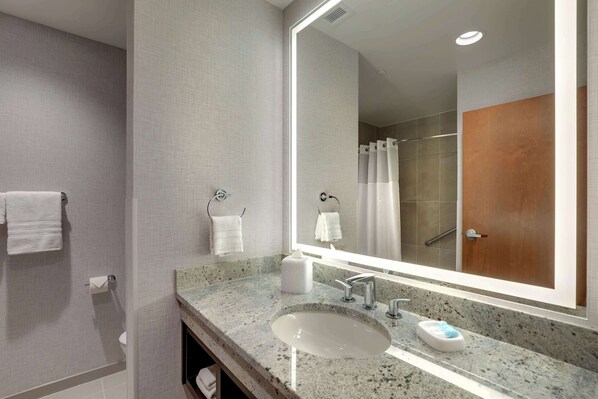Un baño moderno con un espejo grande, encimera de granito, un lavabo y zona de ducha.