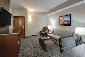 Ett hotellrum med en platt-TV, en soffa, en stol, ett litet bord och en lampa.