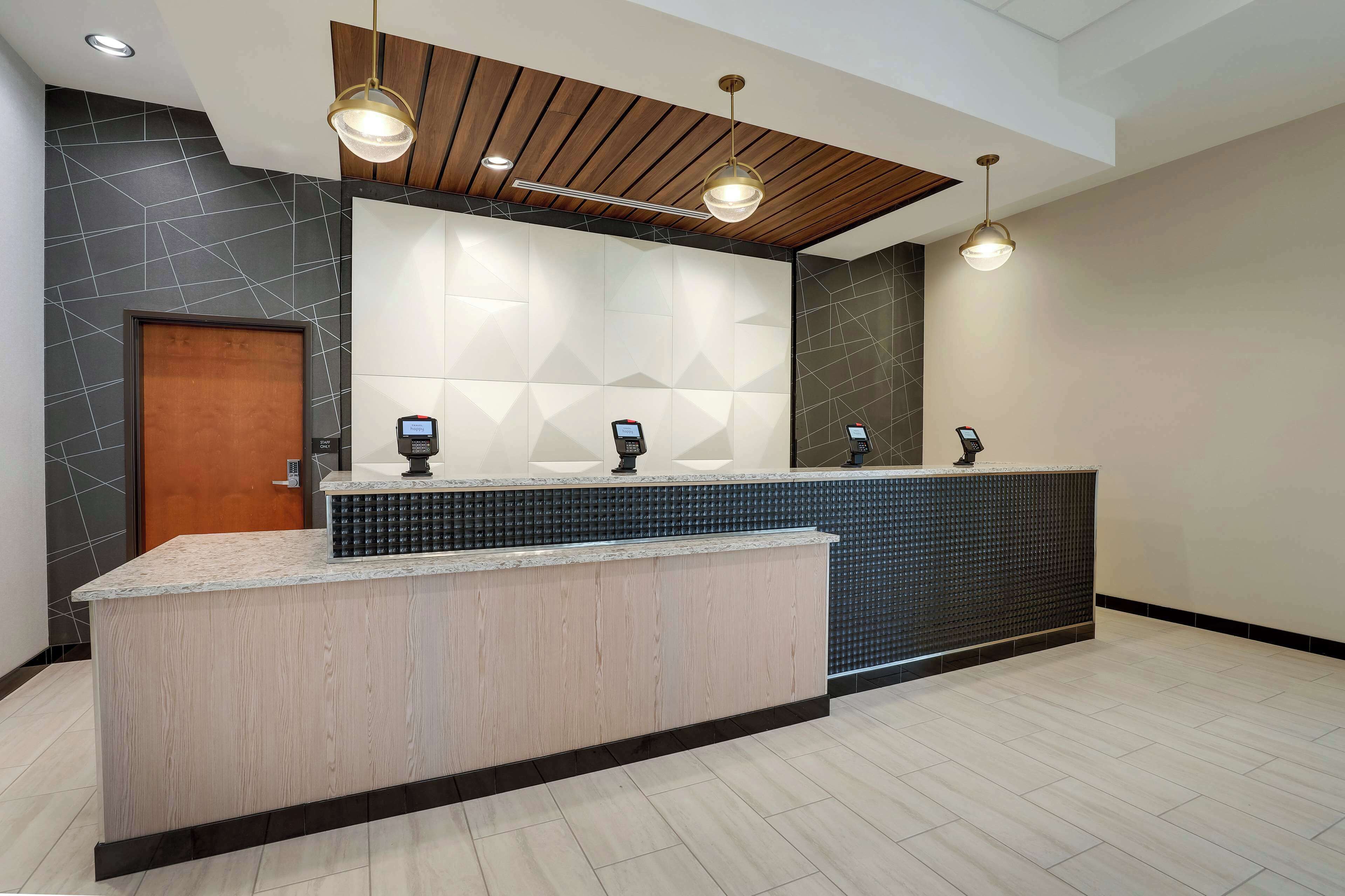 A reception area with a wooden reception desk, a modern geometric wall design, and a ceiling with wooden beams and pendant lighting.