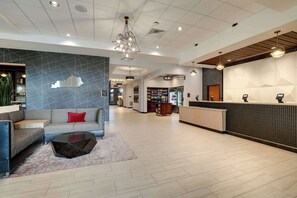 A modern hotel lobby with a reception desk, seating area, and a store.