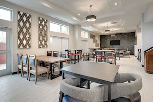 A modern dining area with multiple tables and chairs, a kitchen area with a flat-screen TV, and decorative wall panels.