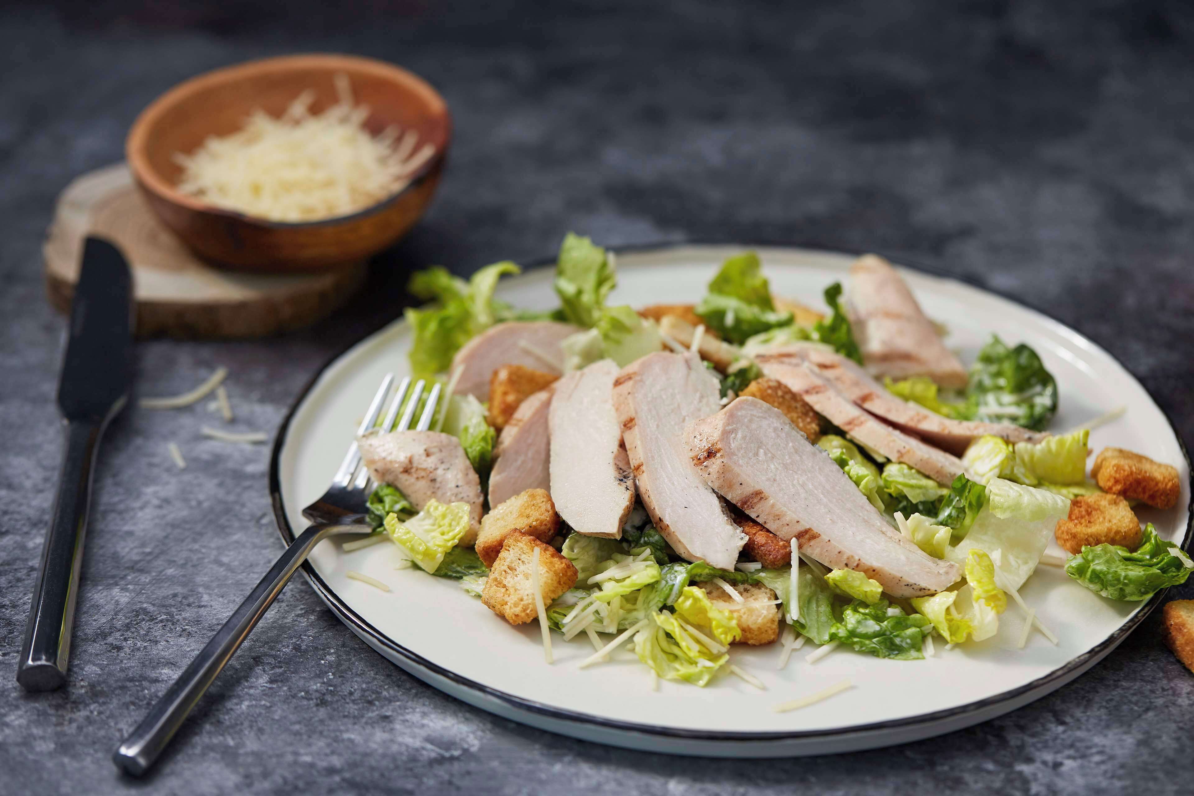 Une assiette de viande tranchée, accompagnée de croûtons et de laitue, posée sur une surface sombre.