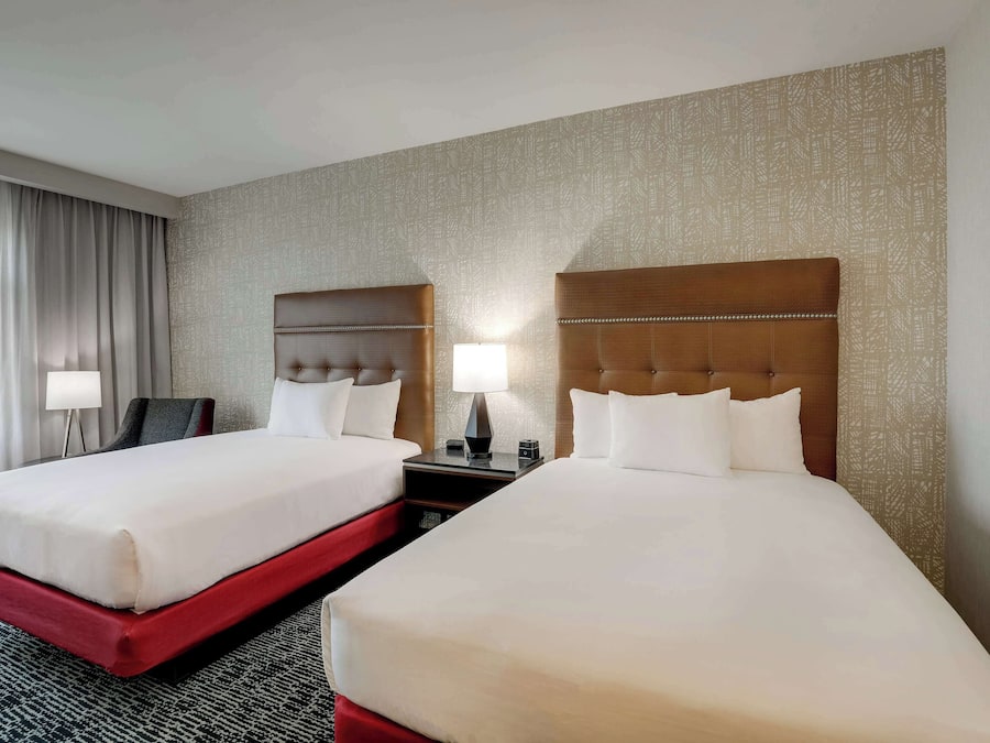 Quarto de hotel com duas camas, uma escrivaninha, uma cadeira e uma luminária.