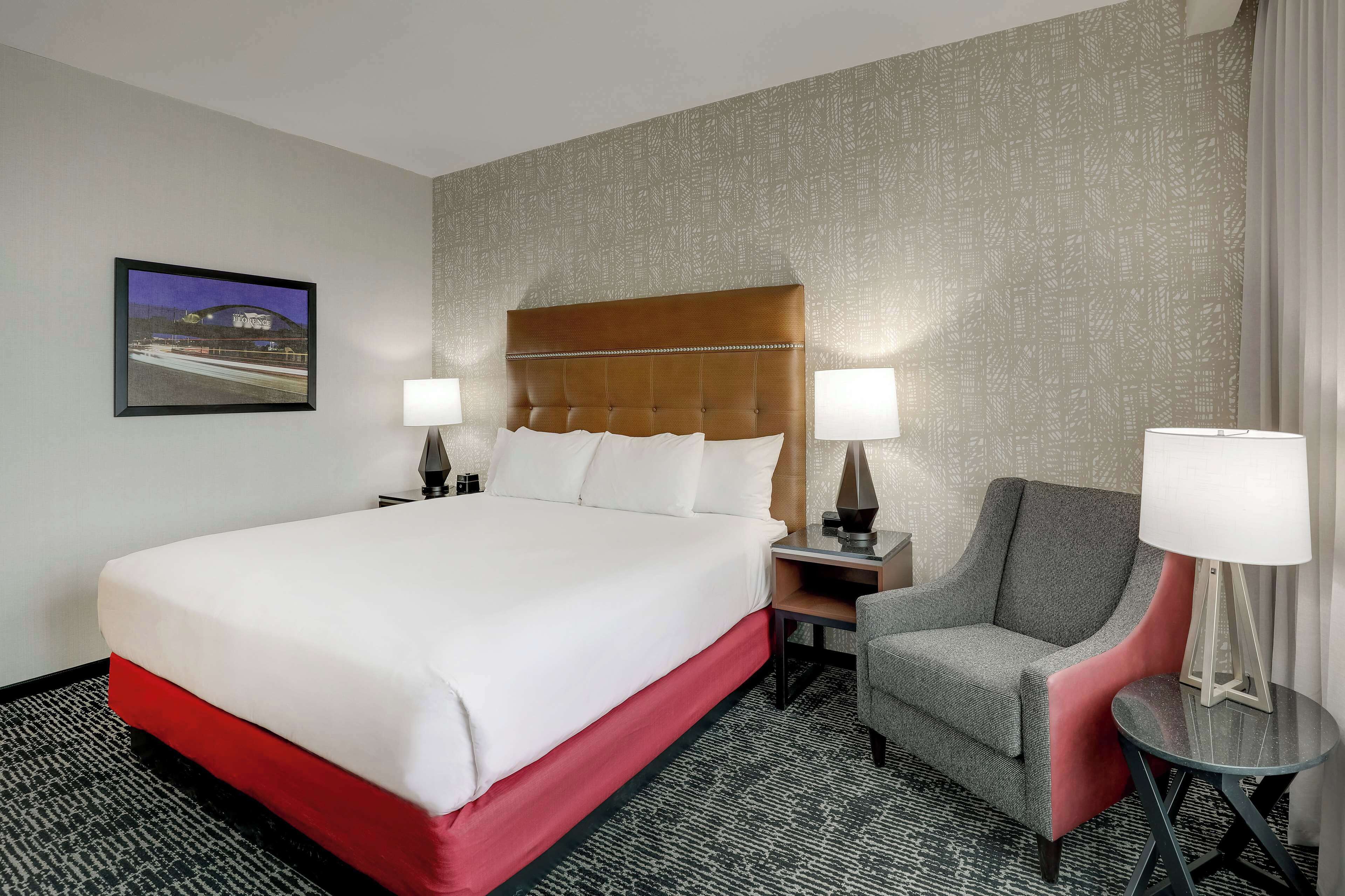 Une chambre d’hôtel avec un grand lit, deux tables de chevet avec des lampes, une chaise et une petite table avec une lampe.