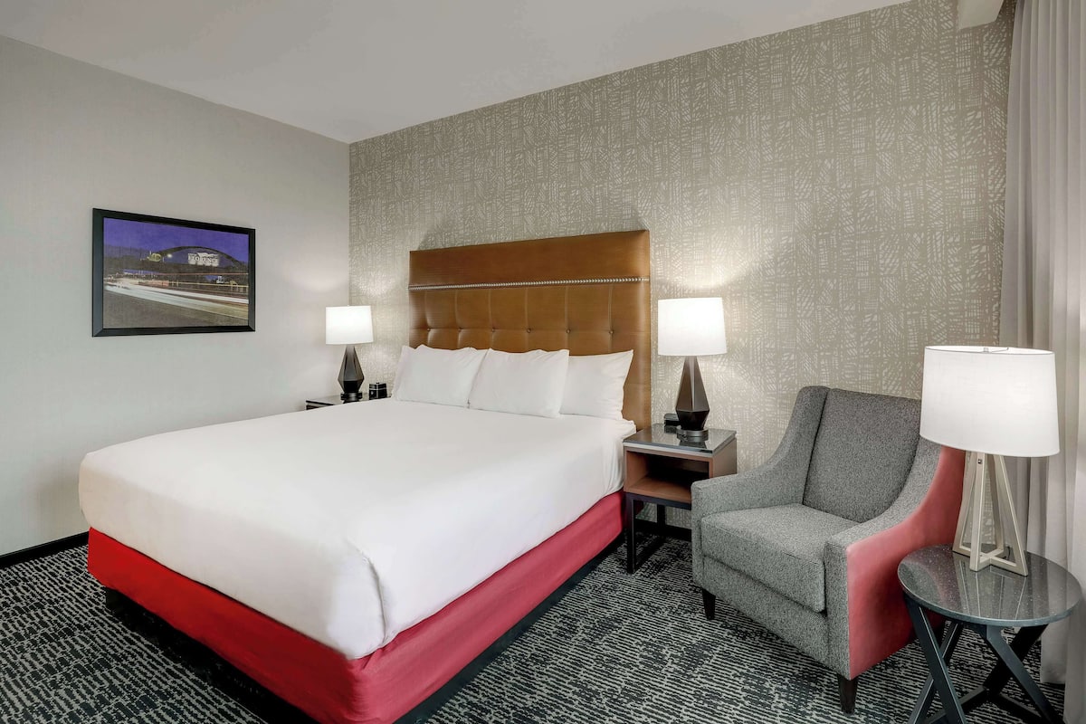 Ein Hotelzimmer mit einem großen Bett, zwei Nachttischen mit Lampen, einem Sessel und einem kleinen Tisch ebenfalls mit einer Lampe.
