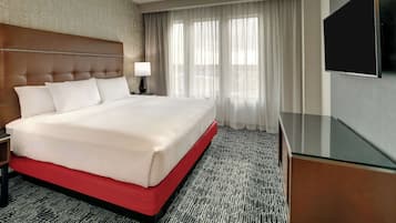 A hotel room with a large bed, a desk, a TV, and a window with curtains.