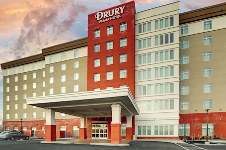 A Drury Plaza Hotel with a prominent red and beige facade, multiple floors, and a covered entrance area.