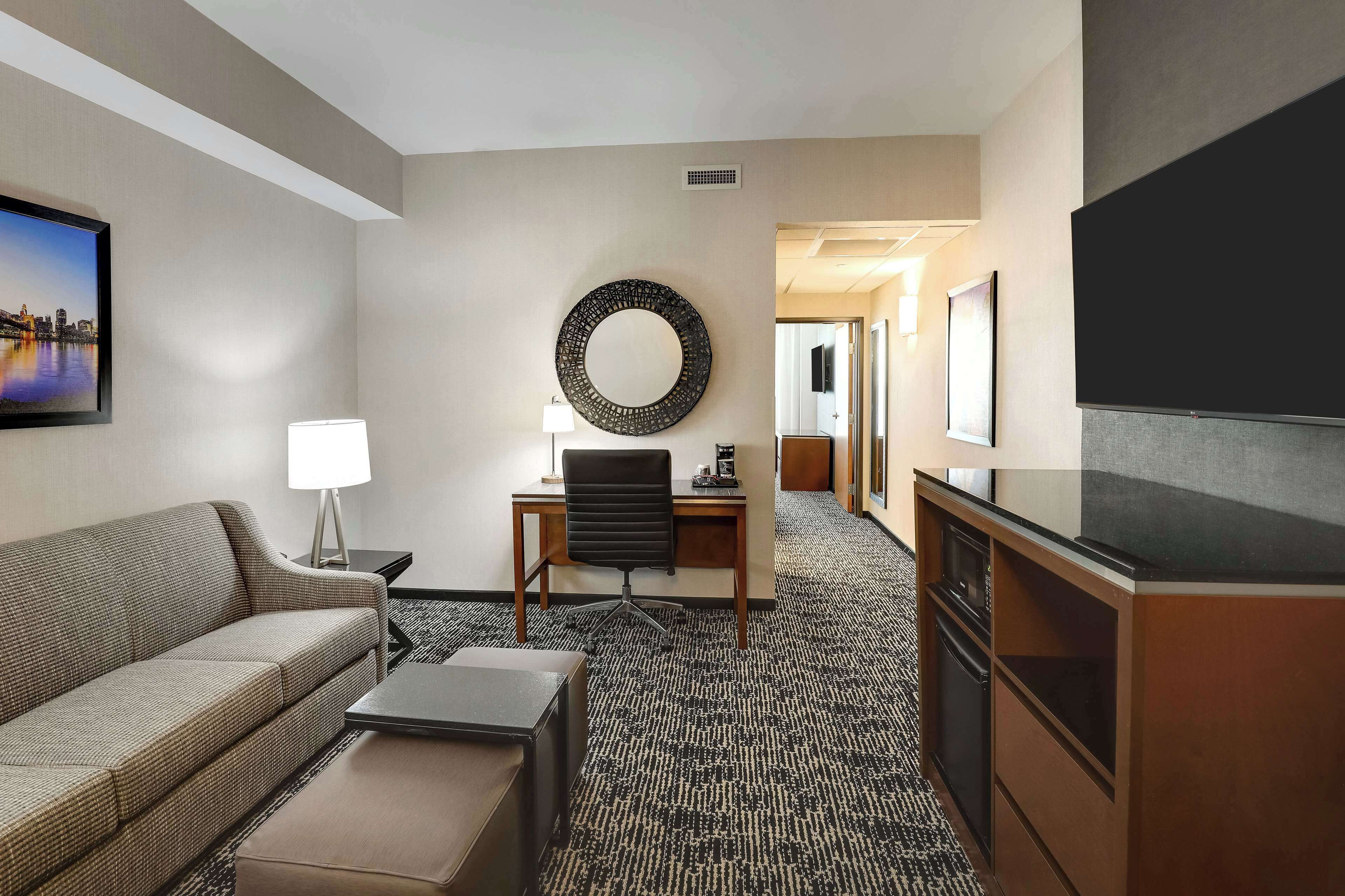 Une chambre d’hôtel équipée d’un canapé, d’un bureau avec une chaise, d’une télévision et d’un grand miroir mural.