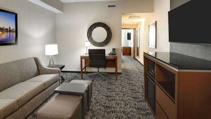 Habitación de hotel con sofá, escritorio con silla, televisión y un espejo grande en la pared.