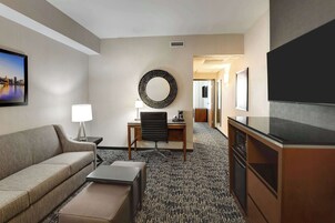 Habitación de hotel con sofá, escritorio con silla, televisión y un espejo grande en la pared.