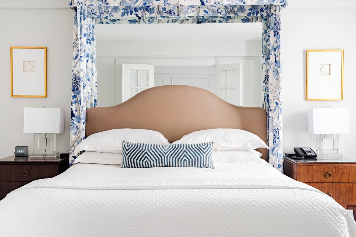 A neatly made bed with white linens, a wooden headboard, and a blue and white patterned pillow. There are two bedside tables with lamps and a phone.