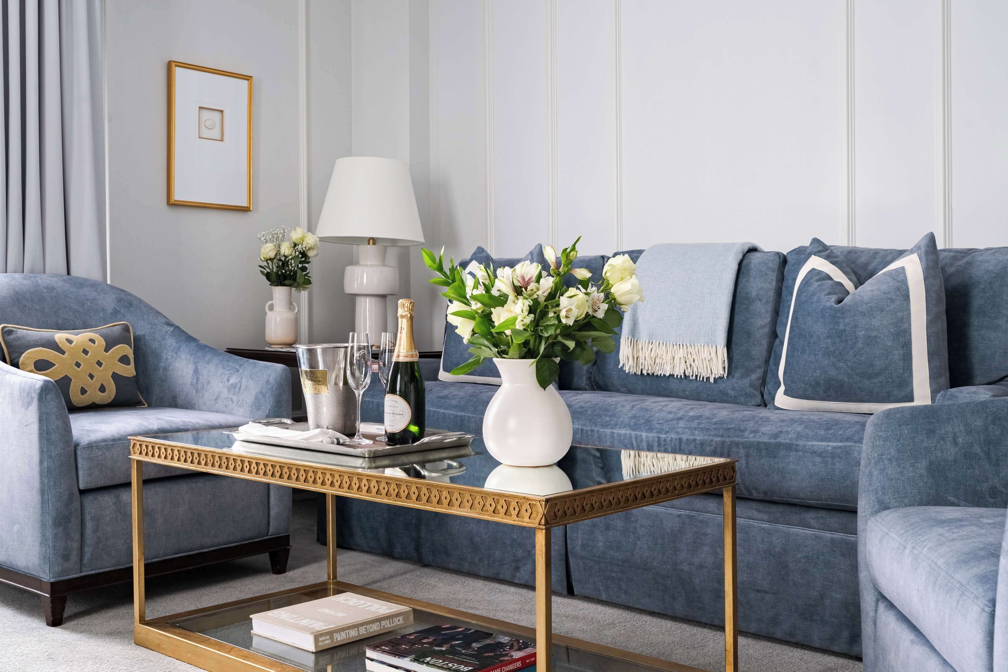A modern living room with a blue sofa, a coffee table, a lamp, and a vase with flowers.