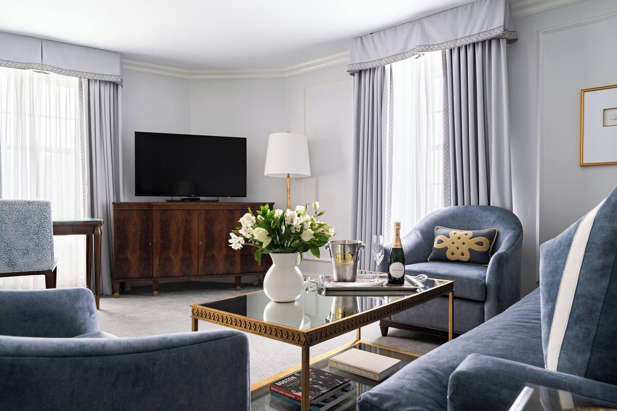A modern living room with a flat-screen TV, a coffee table with a vase of flowers, a sofa, and a chair.