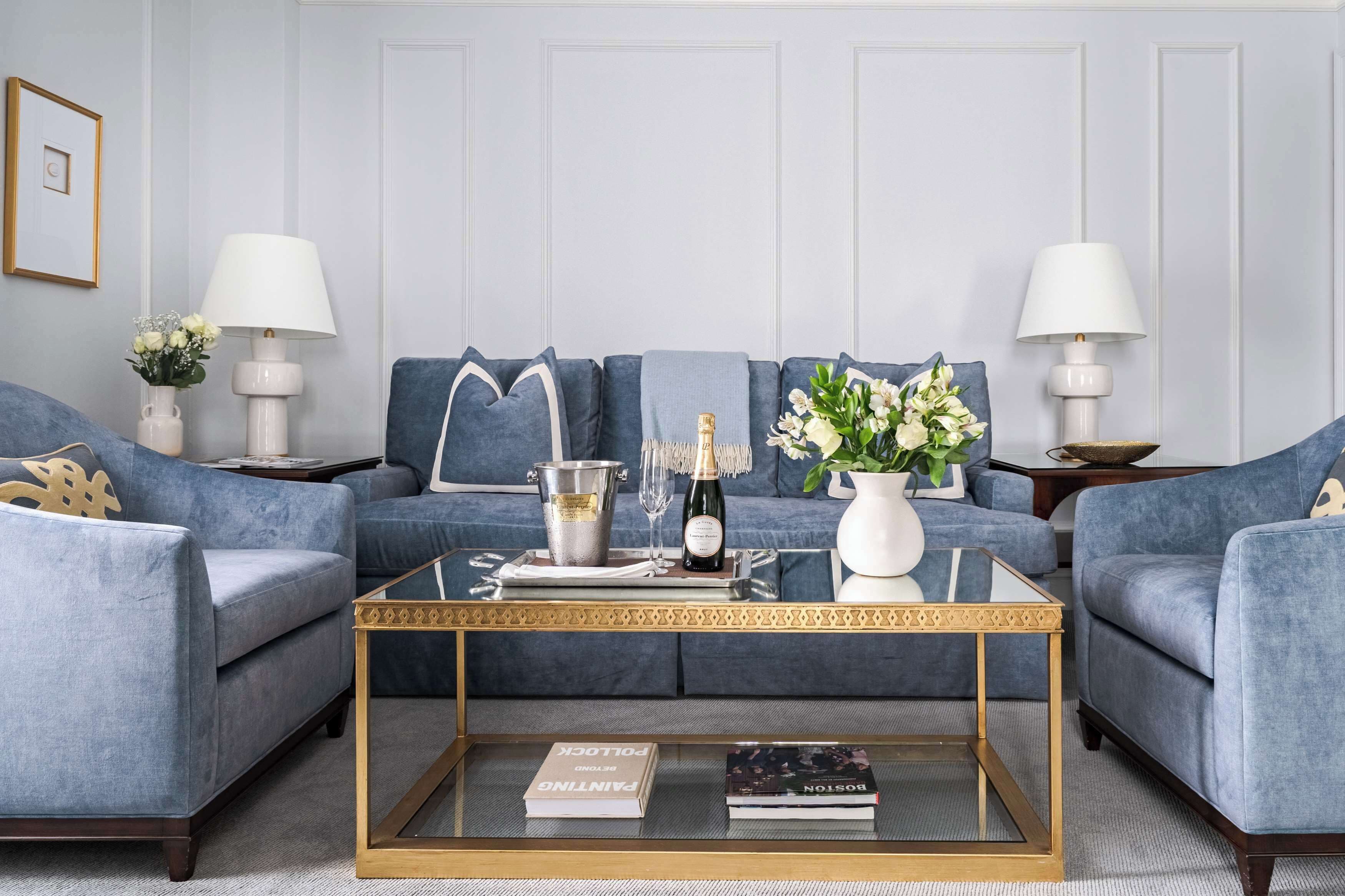 A modern living room with a blue sofa set, a glass coffee table, and two side tables with lamps.