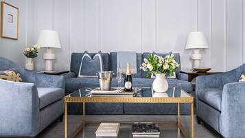 A modern living room with a blue sofa set, a glass coffee table, and two side tables with lamps.