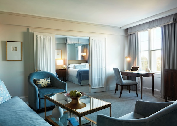 A hotel room with a bed, two chairs, a desk with a laptop, a coffee table, and a view of the outdoors. - The Eliot Hotel (Boston)
