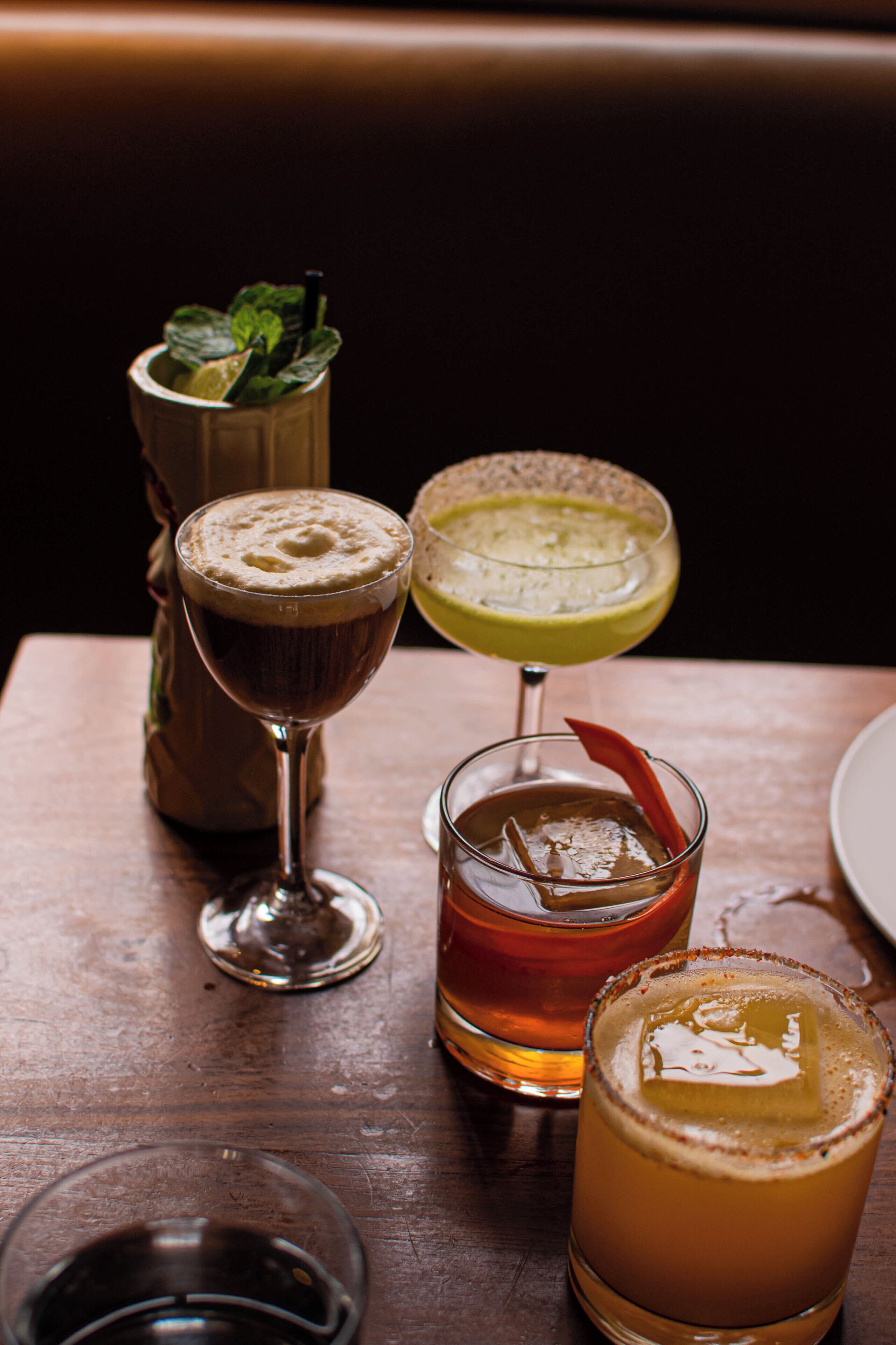 Four glasses of beverages on a wooden table.