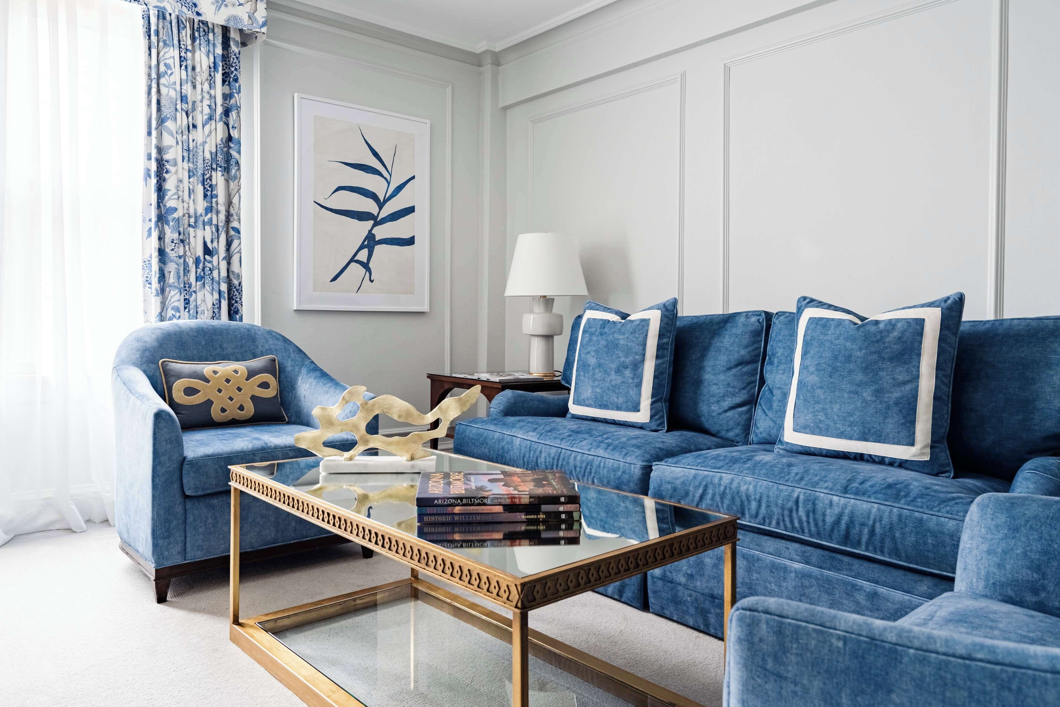A living room with a blue sofa, a glass coffee table, and a framed artwork on the wall.