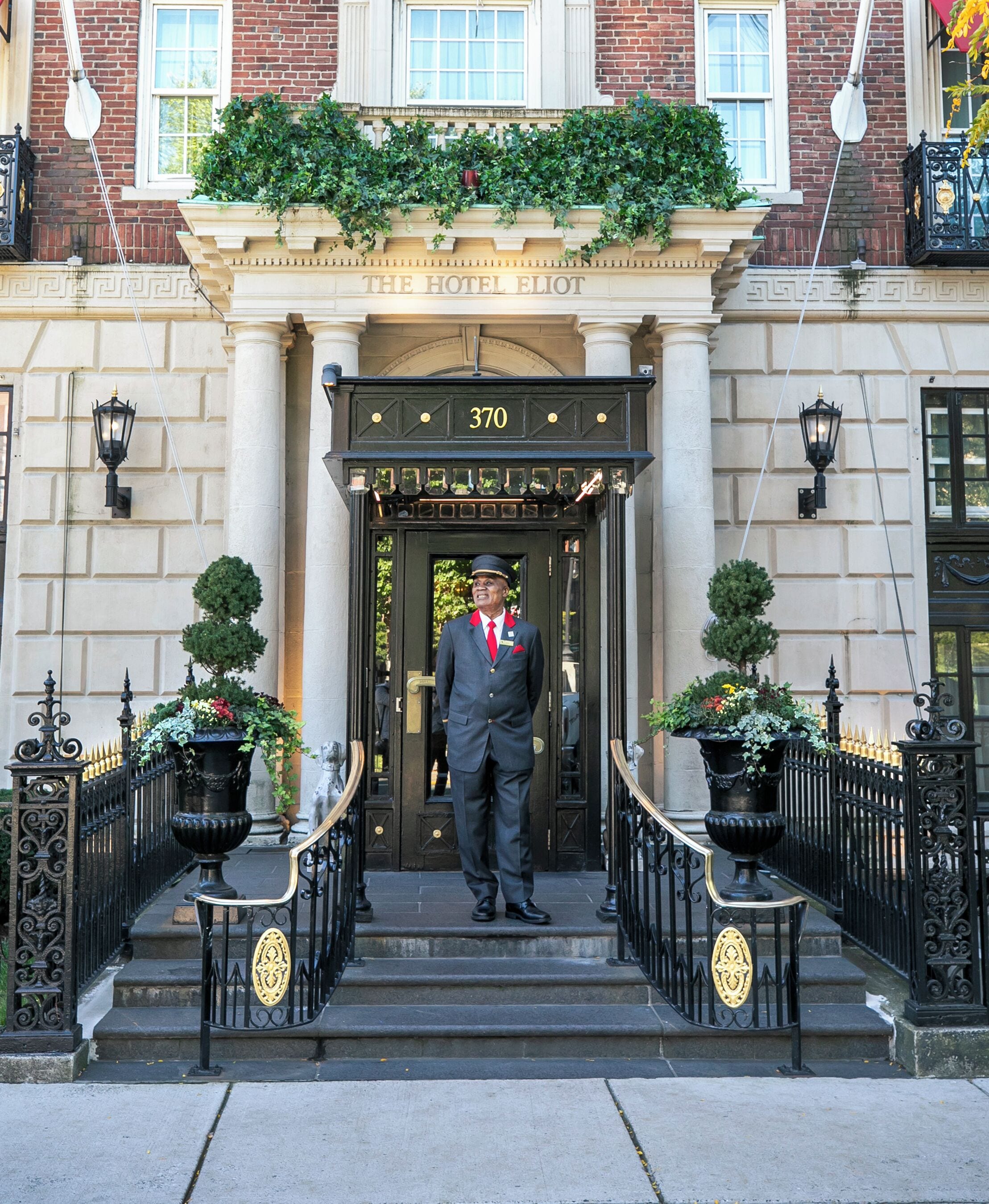 A hotel entrance with a porter standing, a number 370 sign, and a classic architectural style with columns and a balcony.