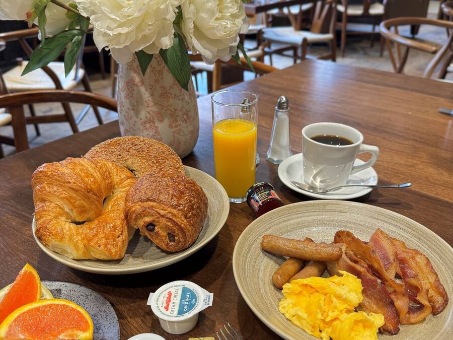A breakfast setting with croissants, eggs, bacon, orange slices, and a vase of flowers.