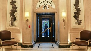 Uma entrada imponente com uma porta preta, duas poltronas de couro marrom e piso de mármore.