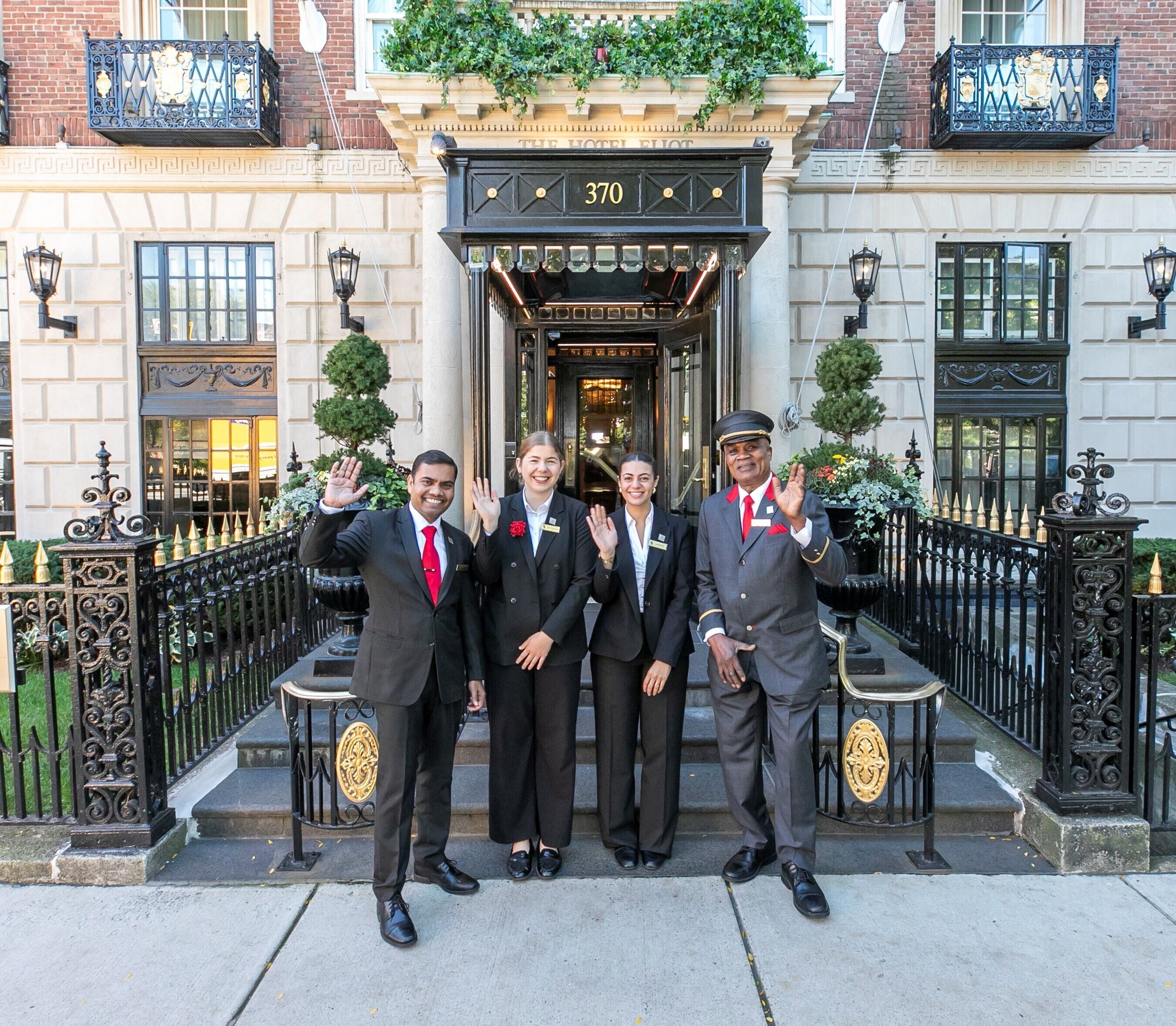 A group of four individuals standing in front of a building with a black entrance and the number 370.