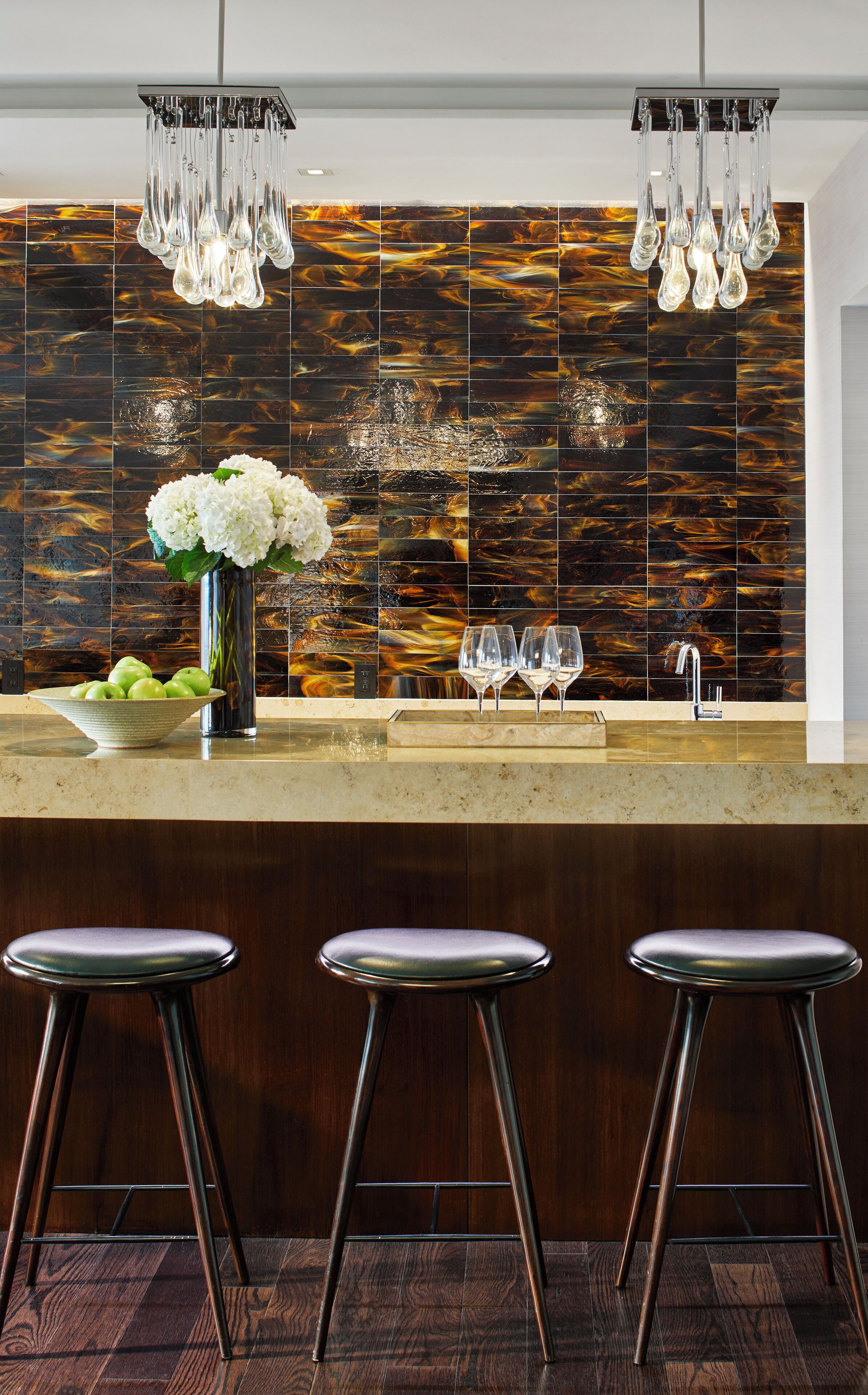 A modern kitchen with a marble backsplash, a central island with stools, and a hanging light fixture.