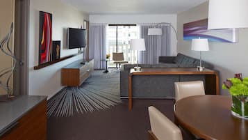 Ein Hotelzimmer mit Fernseher, einer Couch, einem Esstisch und Blick auf die Stadt.