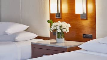 A hotel room with a bed, a bedside table with a vase of white flowers, and wall-mounted light fixtures.