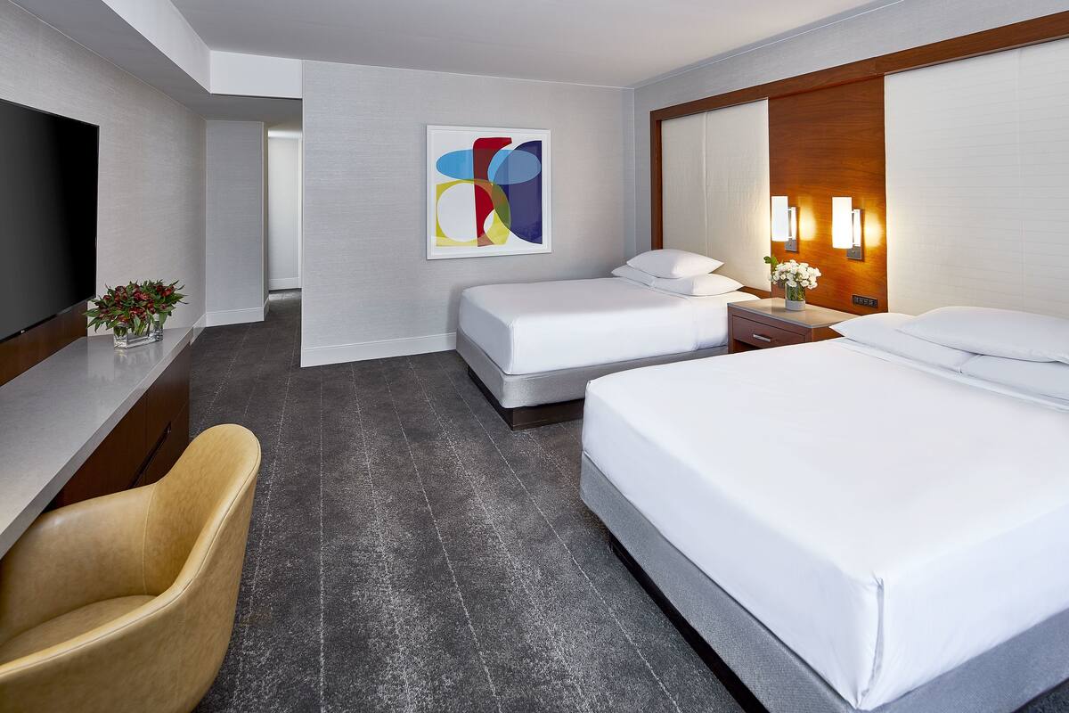 A hotel room with a large bed, a smaller bed, a desk with a TV, a chair, and a painting on the wall.
