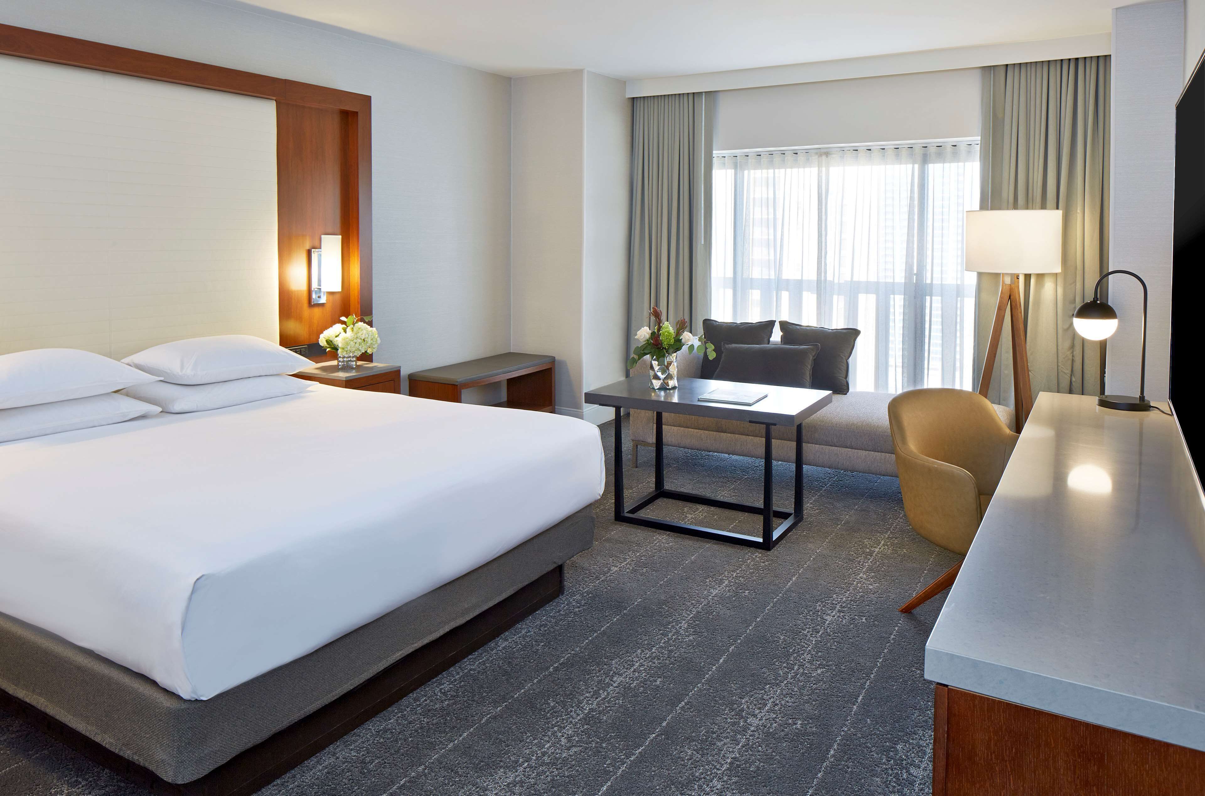 A hotel room with a large bed, a desk, a chair, and a TV.