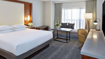 A hotel room with a large bed, a desk, a chair, and a TV.