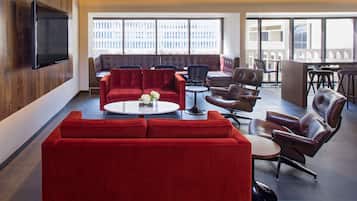 A modern lounge area with a red sofa, leather chairs, a round coffee table, and a flat-screen TV mounted on the wall.