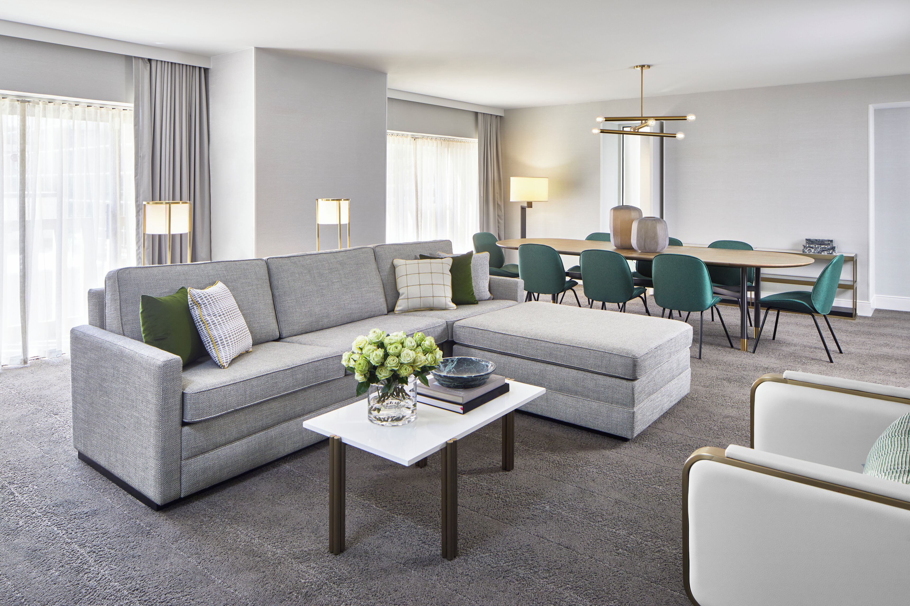 A modern living room with a grey sectional sofa, a white coffee table, and a dining area with green chairs and a wooden table.