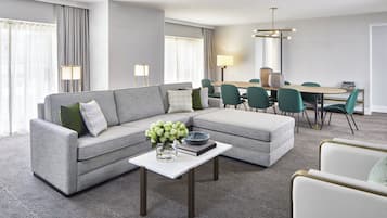 A modern living room with a grey sectional sofa, a white coffee table, and a dining area with green chairs and a wooden table.