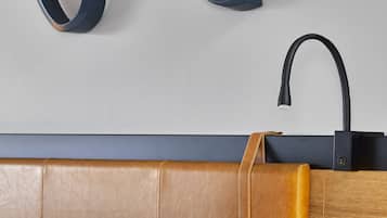 A neatly made bed with white linens, a round gold table lamp, and a wall-mounted black faucet.