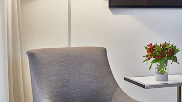 Un fauteuil gris, une lampe sur pied, une petite table avec un vase de fleurs et un tableau encadré au mur.