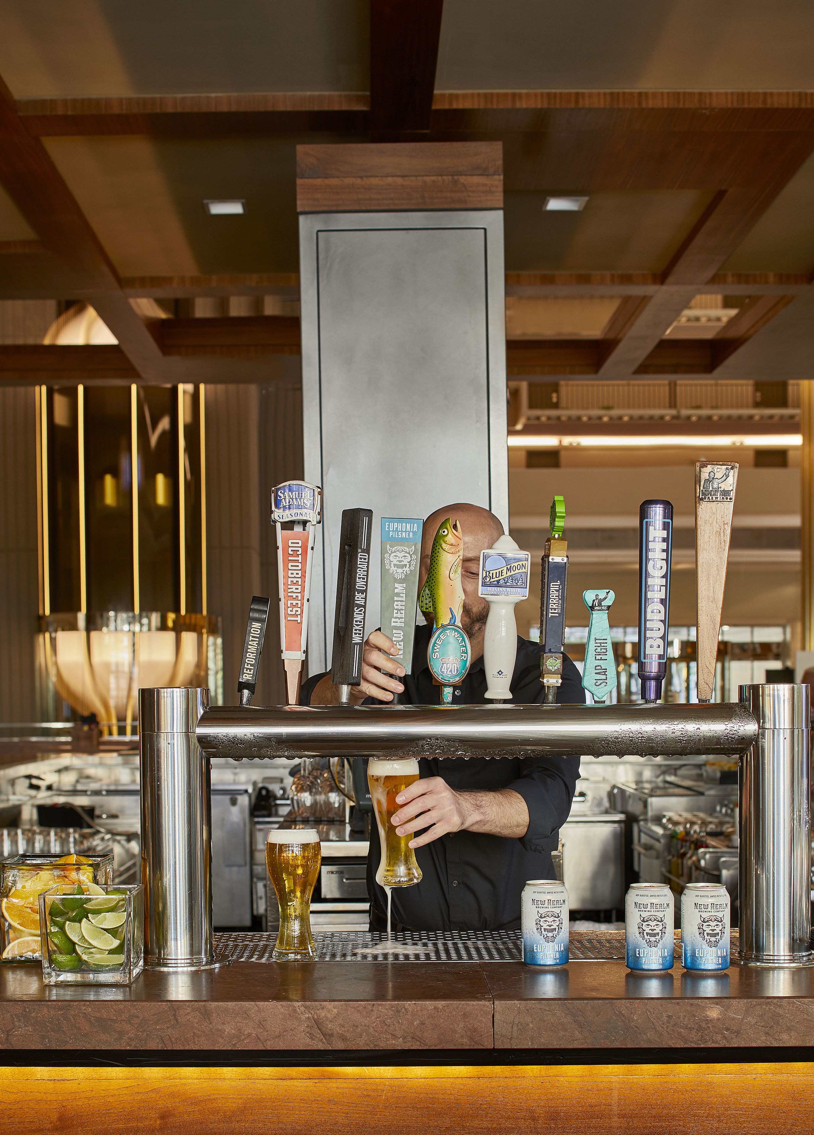 Uma área de bar com várias torneiras de cerveja, um bartender e diversos utensílios de bar.