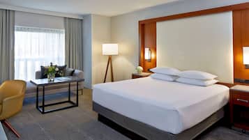 A hotel room with a large bed, a desk, a chair, a lamp, and a nightstand.