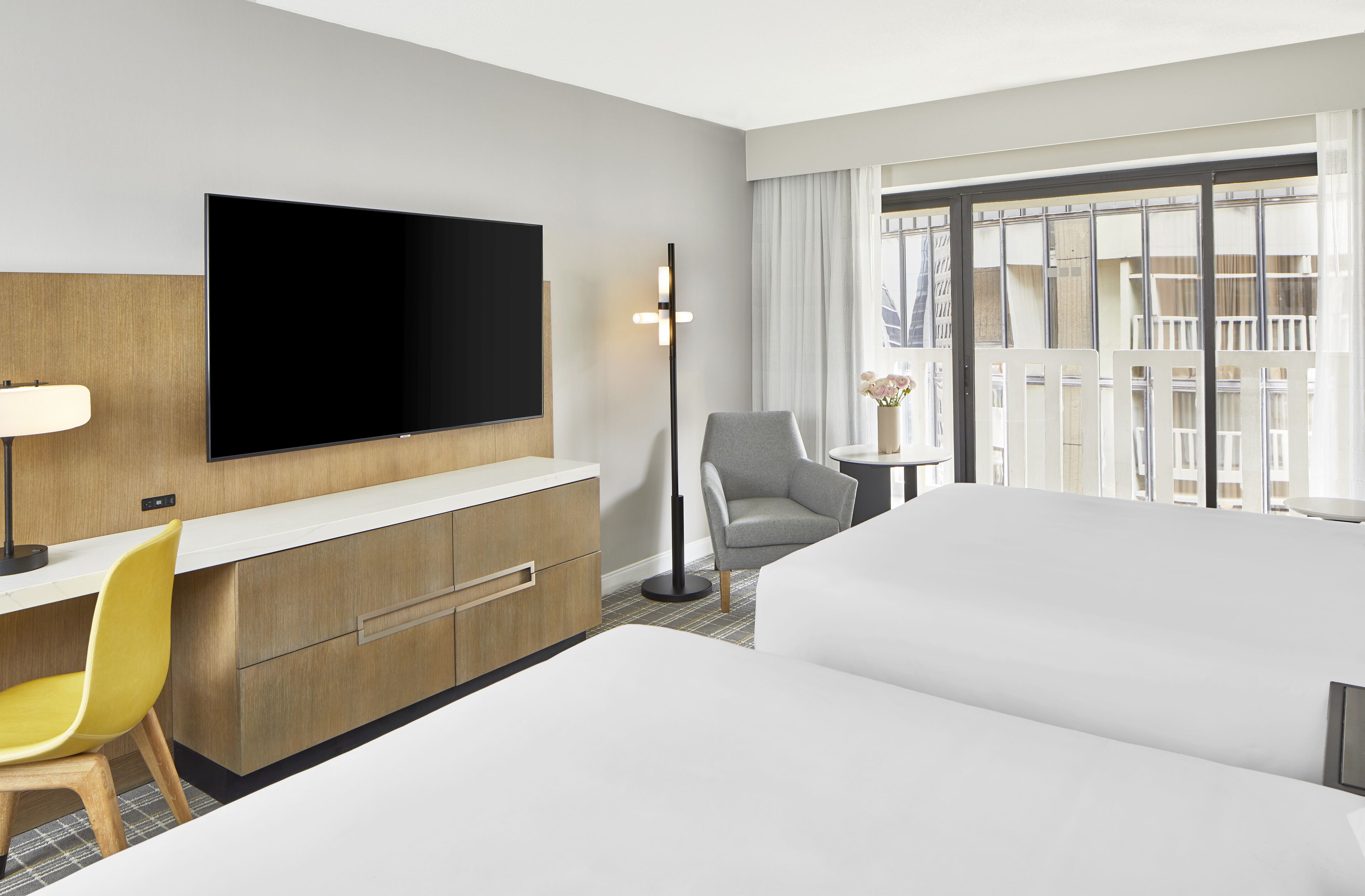 Een hotelkamer met een flatscreen televisie, een bureau met stoel, een bank, een kleine tafel met vaas en een groot raam met gordijnen.