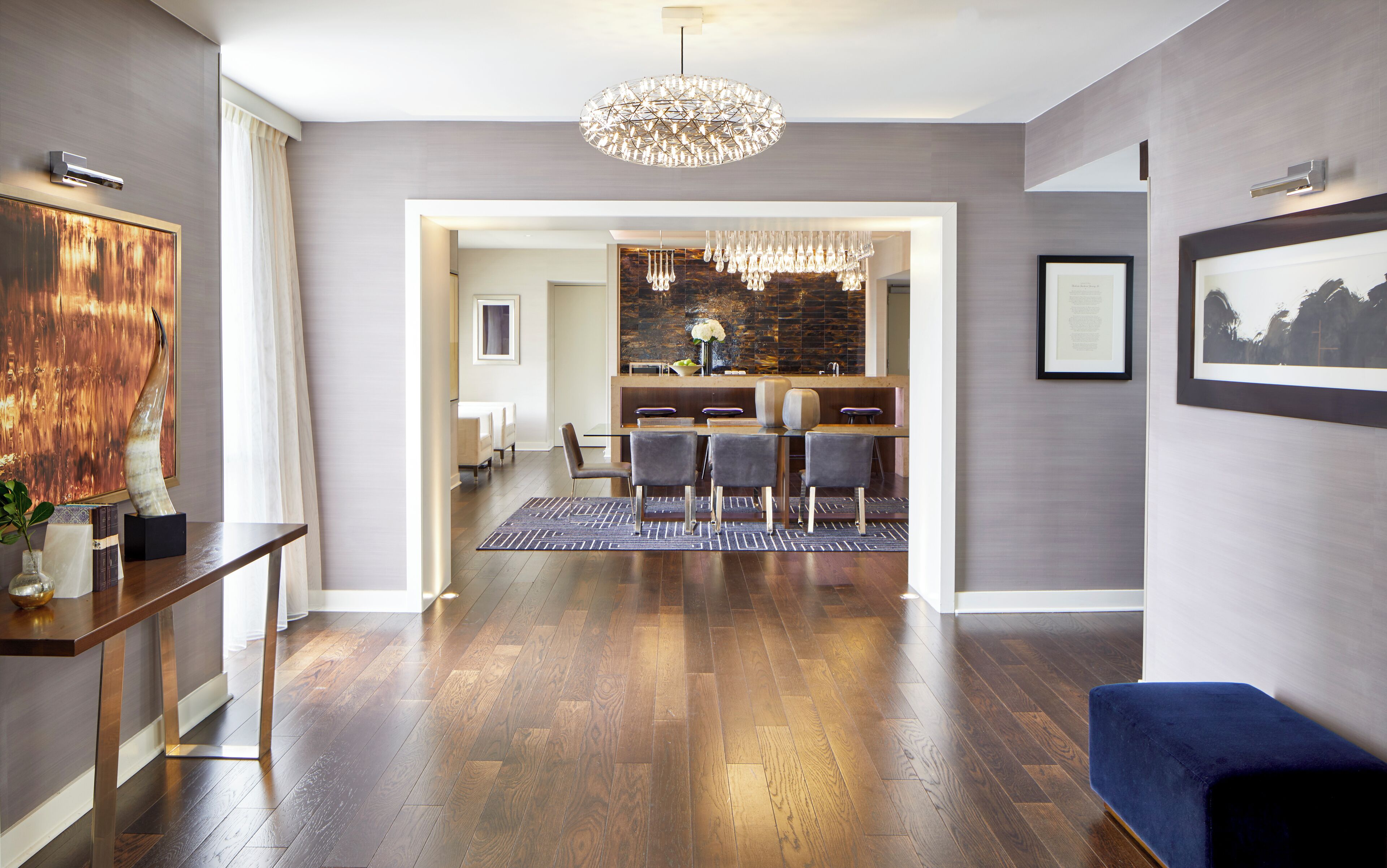 A modern interior with a wooden floor, a dining area with chairs and a table, a blue sofa, and a chandelier.